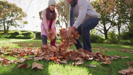 video of happy caucasian grandfather and granddaughter throwing autumn leaves in sunny garden