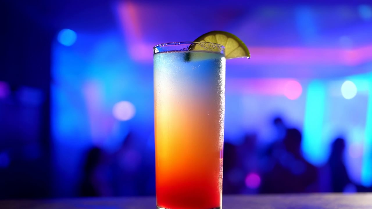 Bicchiere da cocktail a strati vibrante in un nightclub illuminato al neon, bevanda tropicale preparata dal barista con guarnizione di lime.