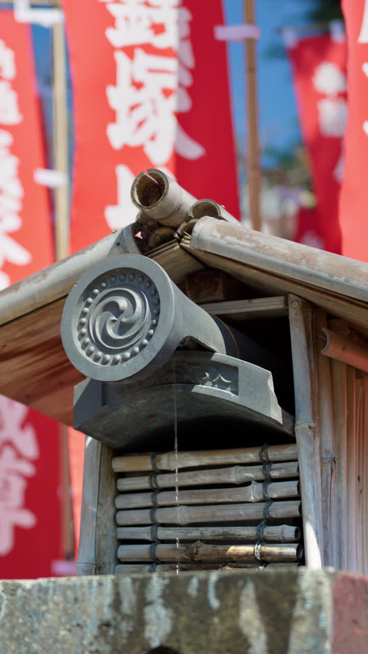 Close up of a small water fountain surrounded by red flags at the Senso-ji temple in Asakusa, Japan. Vertical