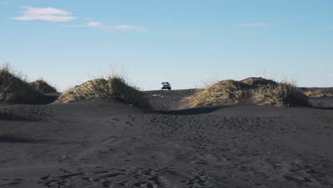 Coche-Estacionado-Entre-Dos-Céspedes-En-Una-Playa-De-Arena-Negra-En-Islandia