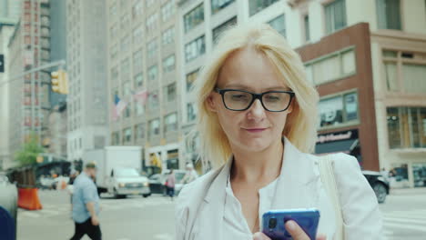 a young woman uses a smartphone against the backdrop of office buildings in downtown manhattan new y