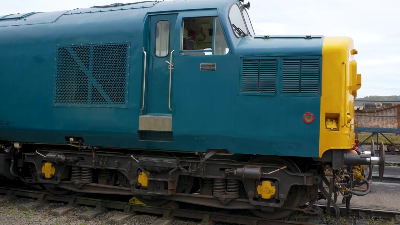 Uma tomada de acompanhamento em close-up mostrando o perfil lateral e os mecanismos de acoplamento de locomotivas diesel britânicas clássicas em um pátio ferroviário. Adequado para documentários de história do transporte e engenharia