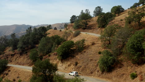 A-car-drives-along-a-road-winding-through-the-dry-Southern-California-landscape-in-the-Red-Mountain-area---aerial-view