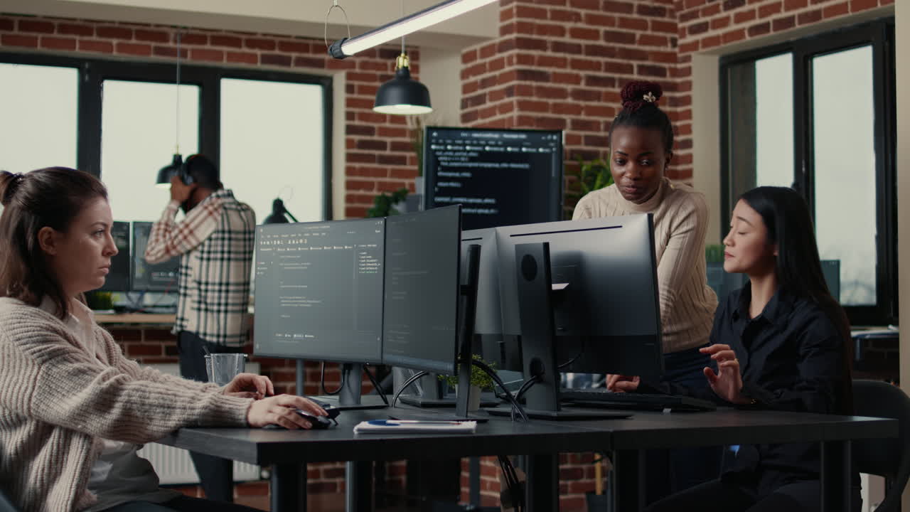 Software engineer typing source code on computer keyboard while colleagues sit down at desk
