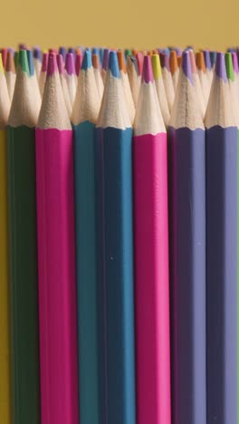 vertical video studio shot of rotating multi-coloured pencils against yellow background 1