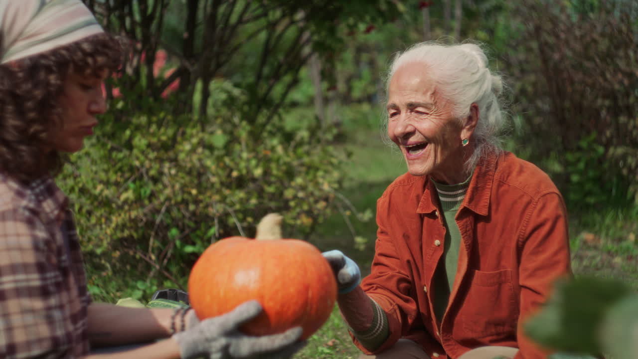 Elderly Woman Discussing Ripe Pumpkin with Granddaughter in Garden
