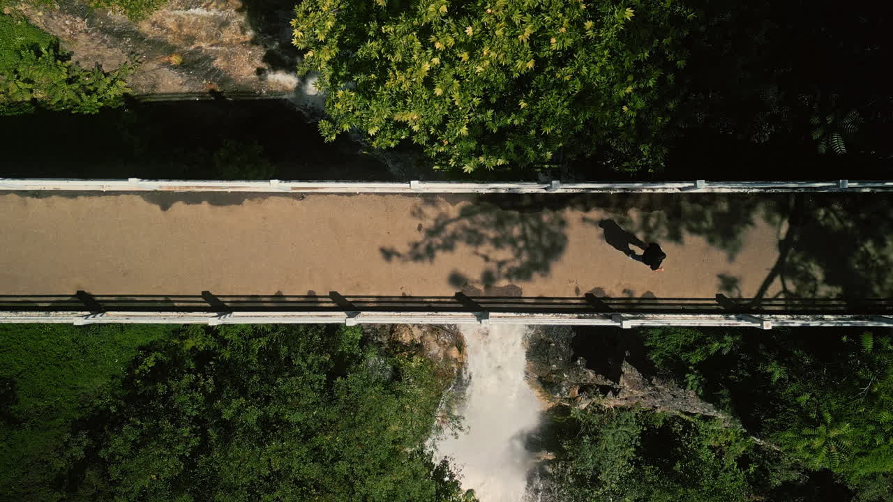 Aerial view of a person walking on a bridge above a waterfall