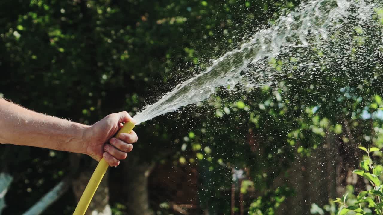 Stream of water spraying from garden hose. Male hand close-up. Slow motion.