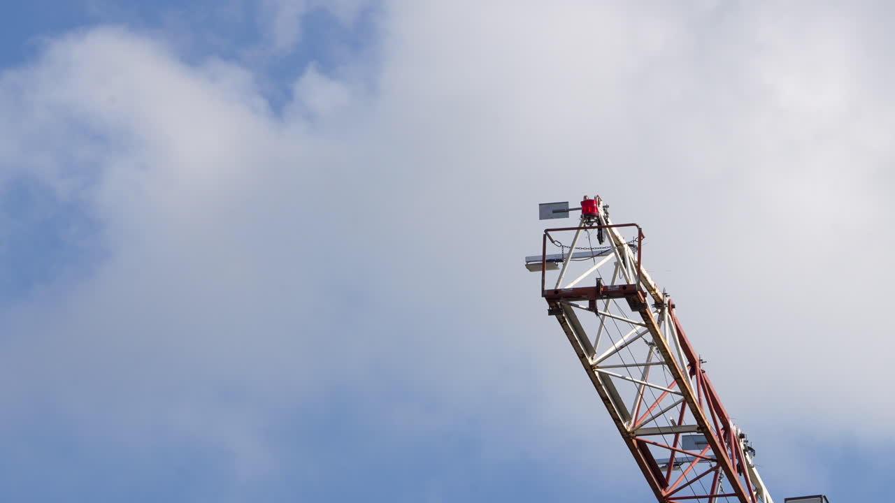 una grúa de construcción alta que se eleva contra un claro cielo azul, con colores rojos y blancos en la maquinaria