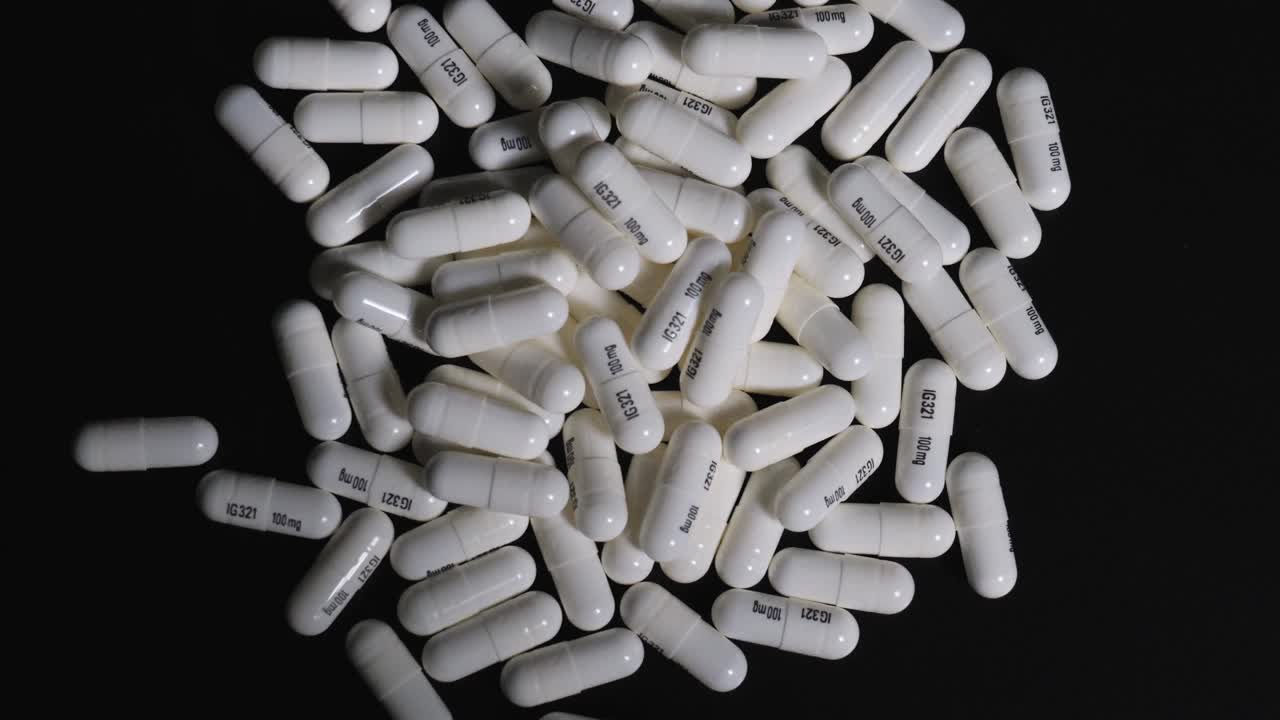 Pillole su prescrizione versate da una bottiglia su un tavolo nero, su uno sfondo scuro