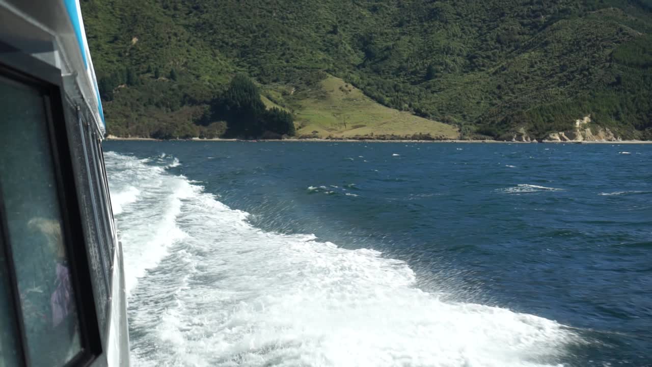 cámara lenta - olas espumosas rompiendo en el costado del barco de crucero en los sonidos de marlborough, nueva zelanda con colinas verdes en el fondo