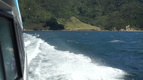 SLOWMO---Foamy-waves-breaking-on-side-of-cruise-boat-in-Marlborough-Sounds,-New-Zealand-with-green-hills-in-background