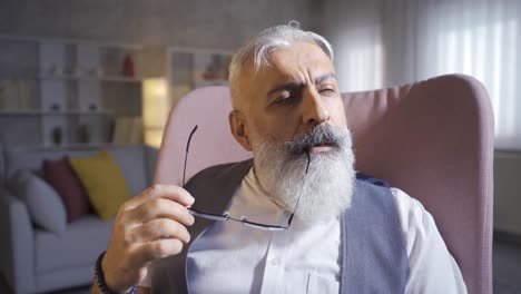 the old man is thinking, playing with his beard and glasses.