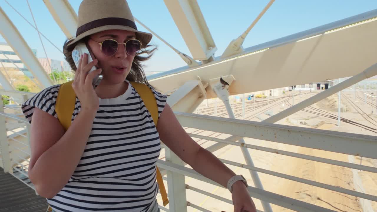 A woman is talking on her cell phone while wearing a hat and sunglasses
