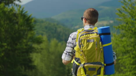 a tourist man with a yellow backpack looks forward to a beautiful mountain landscape with a forest i