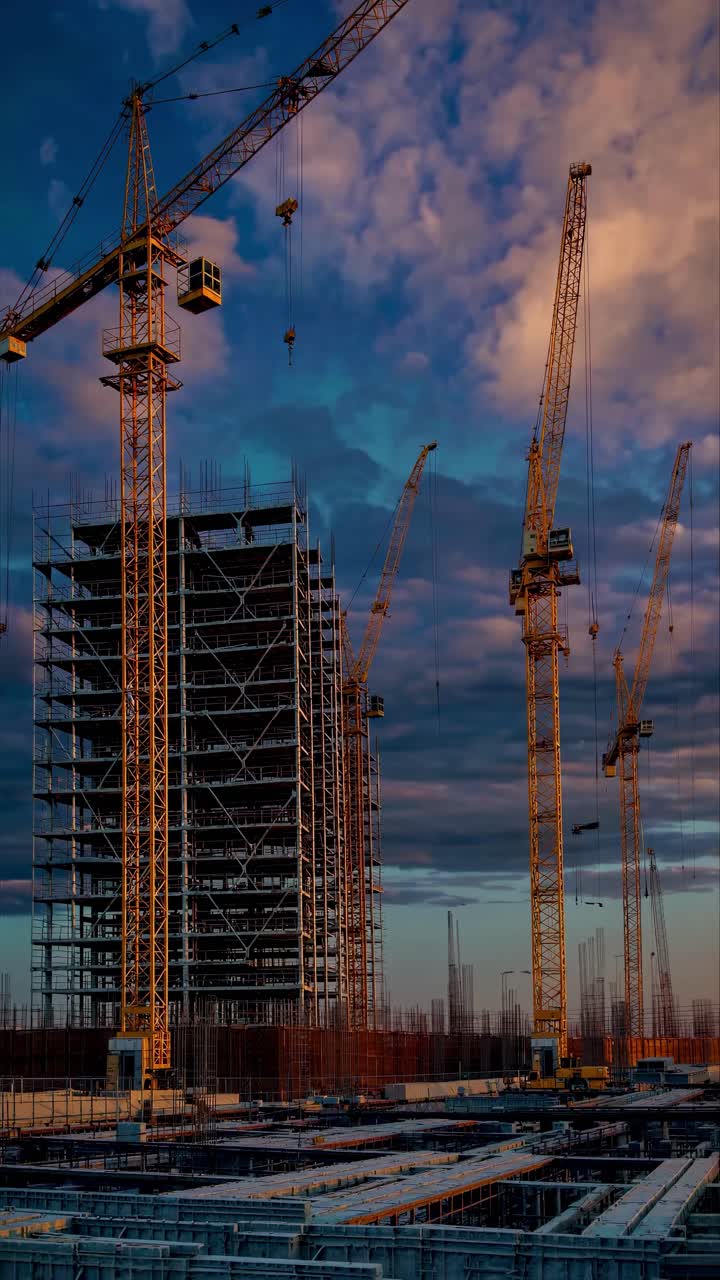A low-angle video shot of towering cranes and a building under construction, set against a dramatic