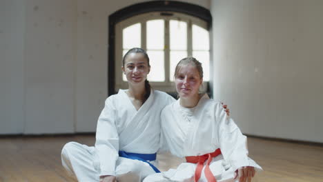 front view of smiling martial artists sitting and hugging in gym