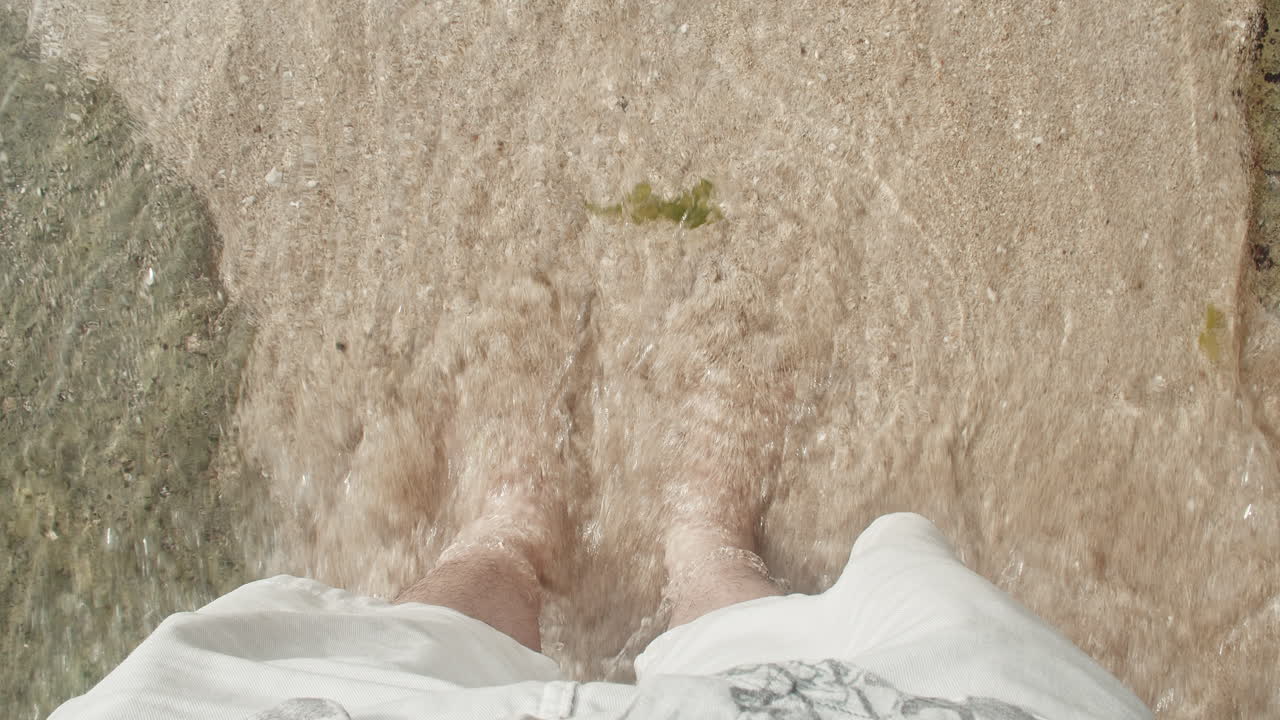 모래 바닥이 있는 맑은 바닷물에 맨발로 서있는 남성의 상위 뷰