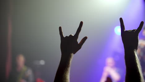 energetic music concert crowd experiencing collective excitement, raising hands and making enthusiastic gestures under vibrant purple stage lighting with blue balloon floating overhead
