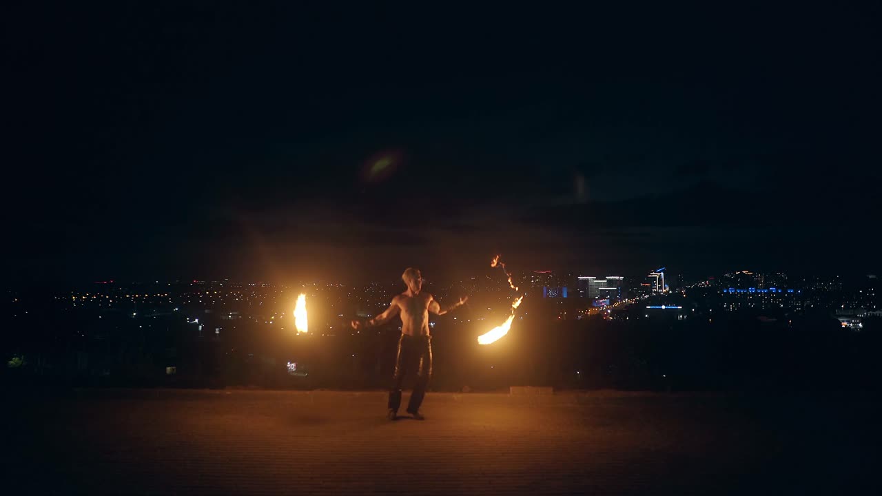 jóvenes hombres rubios bailan con dos antorchas encendidas en medio de la noche con el horizonte de la ciudad en fondo negro