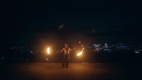 jóvenes hombres rubios bailan con dos antorchas encendidas en medio de la noche con el horizonte de la ciudad en fondo negro