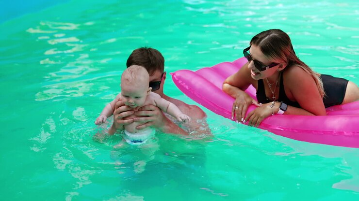 Happy family having a day off in the pool. Caucasian parents are resting in water with their baby on hot summer day.