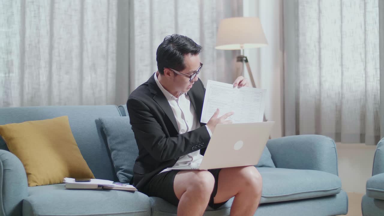 재과 쇼트를 입은 아시아 사업가 가 집에 있는 노트북에서 작업 서류를 제시하고 있다