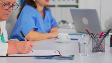 Close-up-of-elderly-woman-medic-taking-notes-on-clipboard