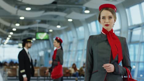 Portrait-Shot-Of-The-Young-Blonde-Pretty-Stewardess-In-The-Stylish-Uniform-Standing-In-The-Airport-Hall-And-Smiling-Happily