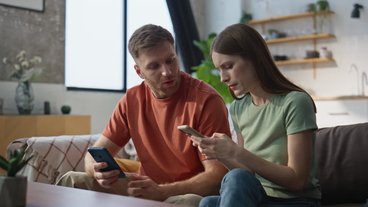 Concerned couple discussing message looking mobile phones at couch closeup