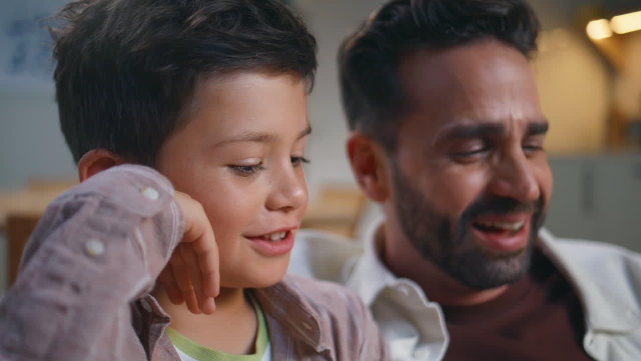 Focused boy looking movie with father evening apartment closeup. Family weekend