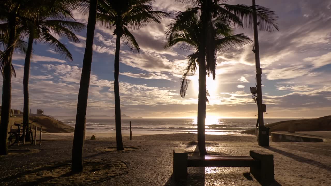 Timelapse de un amanecer a contraluz en el bulevar de Arpoador con la playa del Diablo y palmeras silueteadas en Río de Janeiro contra un cielo azul con nubes