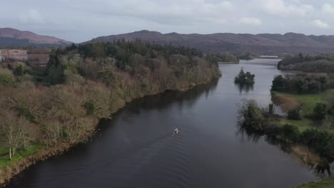 Small-fishing-boat-travelling-up-scenic-river-4K-AERIAL