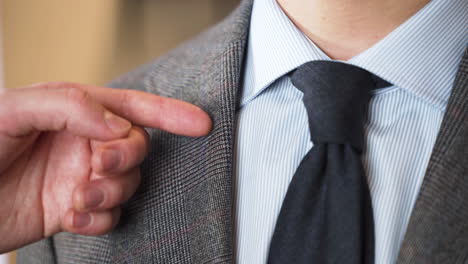 tailor pointing out lapel cut of tweed jacket on customer, close up