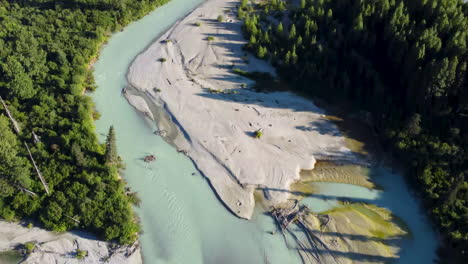 aerial drone panning up on light blue river to reveal pine tree covered mountainside pacific ranges canada bc 4k