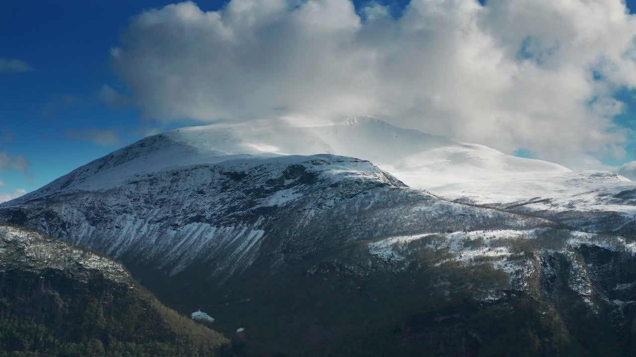 Nuvole bianche e soffici che si stagliano sopra la cima della montagna innevata.