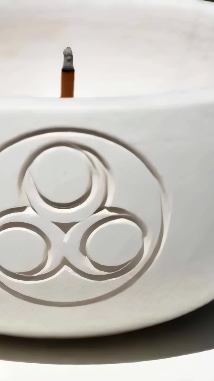 Vertical video: Smoldering ash tip incense stick sending smoke above white ceramic bowl ring motif