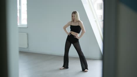 fit girl in black clothes performing contemporary. female dancer shows flowing motions, body and hands waves at white room. modern ballet dance choreography. young woman is moving smoothly