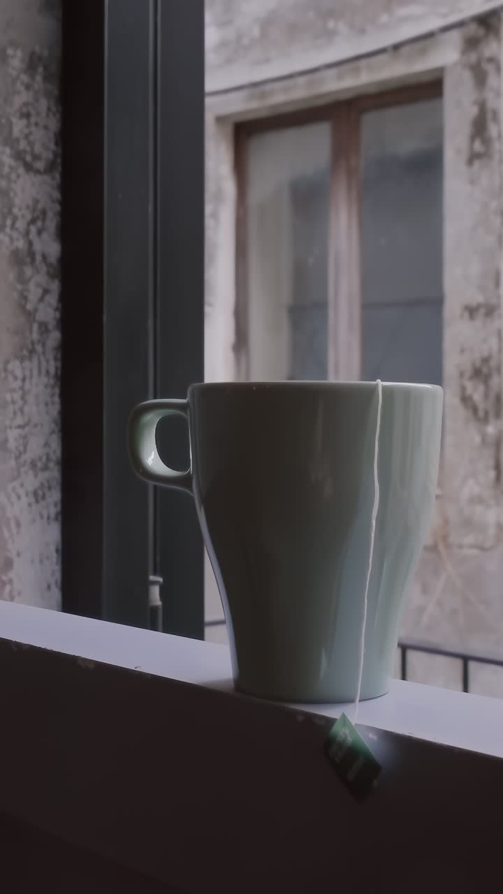 el vapor gira desde una taza de té o café prístina en la repisa del balcón. la luz de la mañana arroja sombras suaves a través de la pared texturizada, creando una escena contemplativa en cámara lenta cinematográfica.