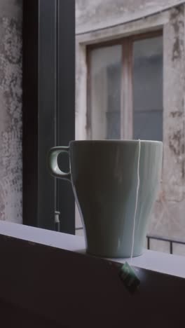 steam swirls from pristine tea or coffee cup on weathered balcony ledge. morning light casts gentle shadows across textured wall, creating contemplative scene in cinematic slow motion.