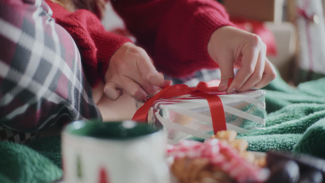 primer plano de una mujer haciendo un lazo de cinta en un regalo de navidad envuelto