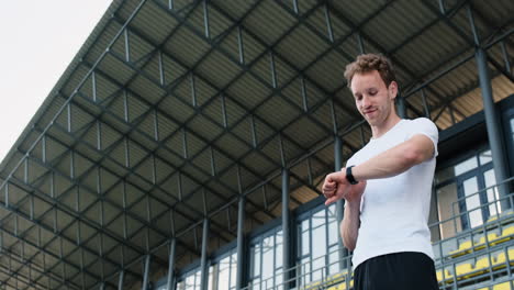 happy sportive man checking his smartwatch before outdoor training in the stadium