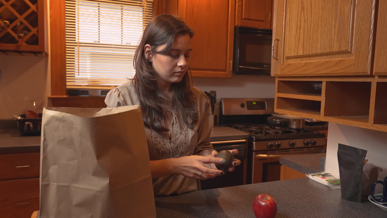 una mujer joven sacando productos de la bolsa de comestibles. poniendo verduras en la mesa.