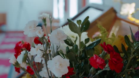 primer plano de un exuberante arreglo floral con claveles rojos y flores blancas, contra un fondo de enfoque suave que sugiere iconos de la iglesia