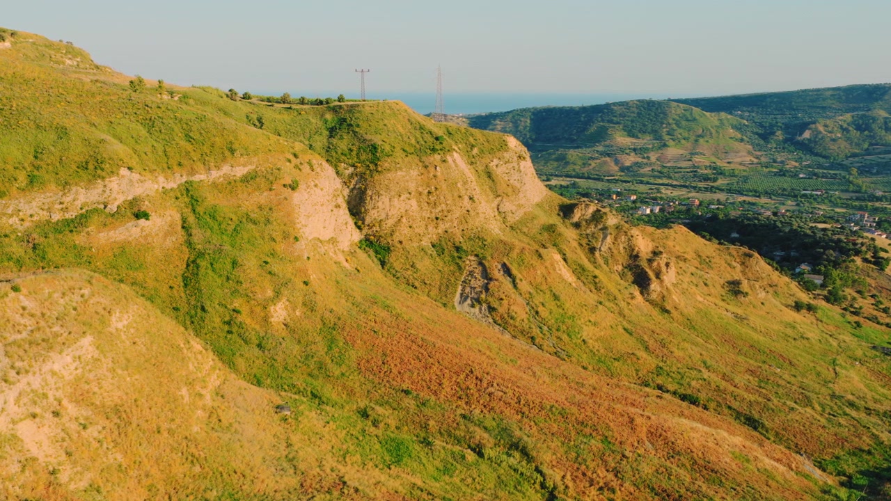 Vista aerea di colline verdi e dorate con mare e villaggio in lontananza