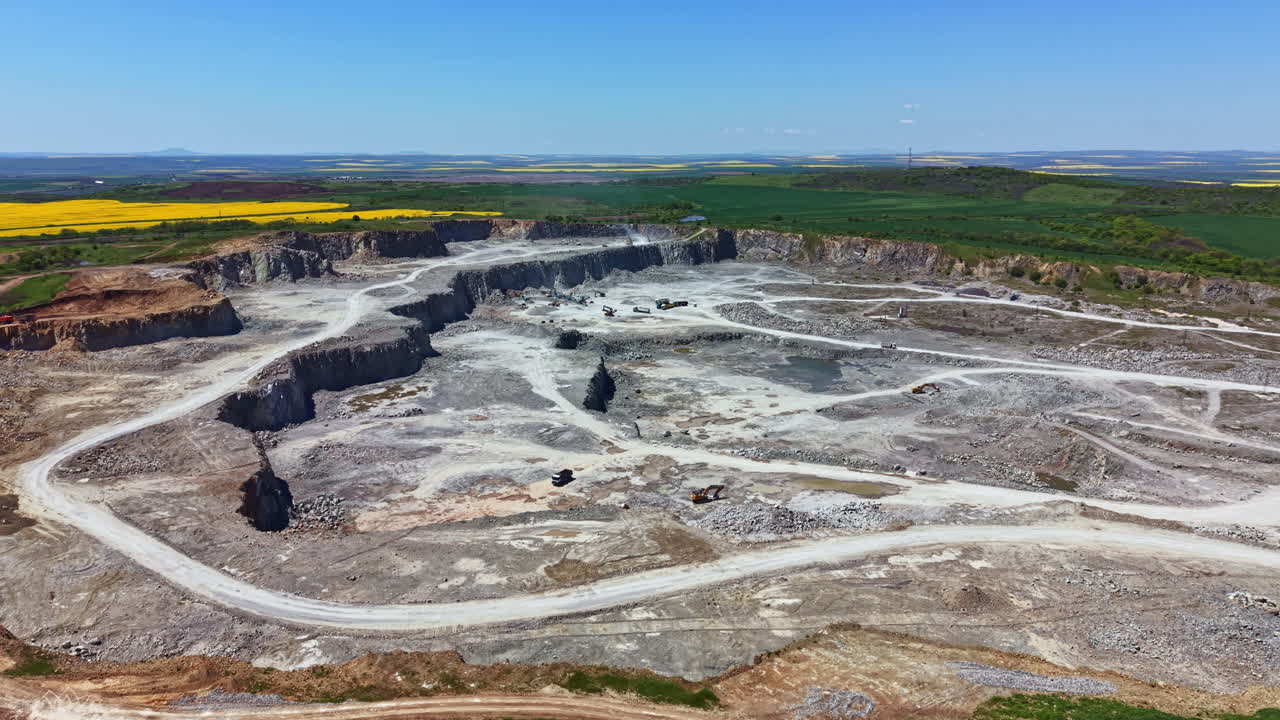 Sito industriale che opera in una cava in una zona rurale con campi verdi e colline visibili sullo sfondo durante il giorno.