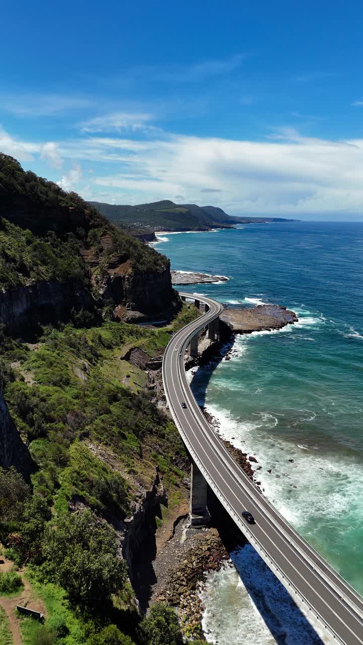 Aerial pullback of Sea Cliff Bridge winding along coastal cliffs in New South Wales, Australia, vertical