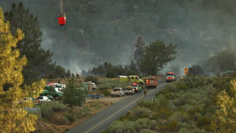 helicopter with water bucket landing on road, distant view, first responders on site for wildfire, firetrucks with flashing lights, kern river, june 2020