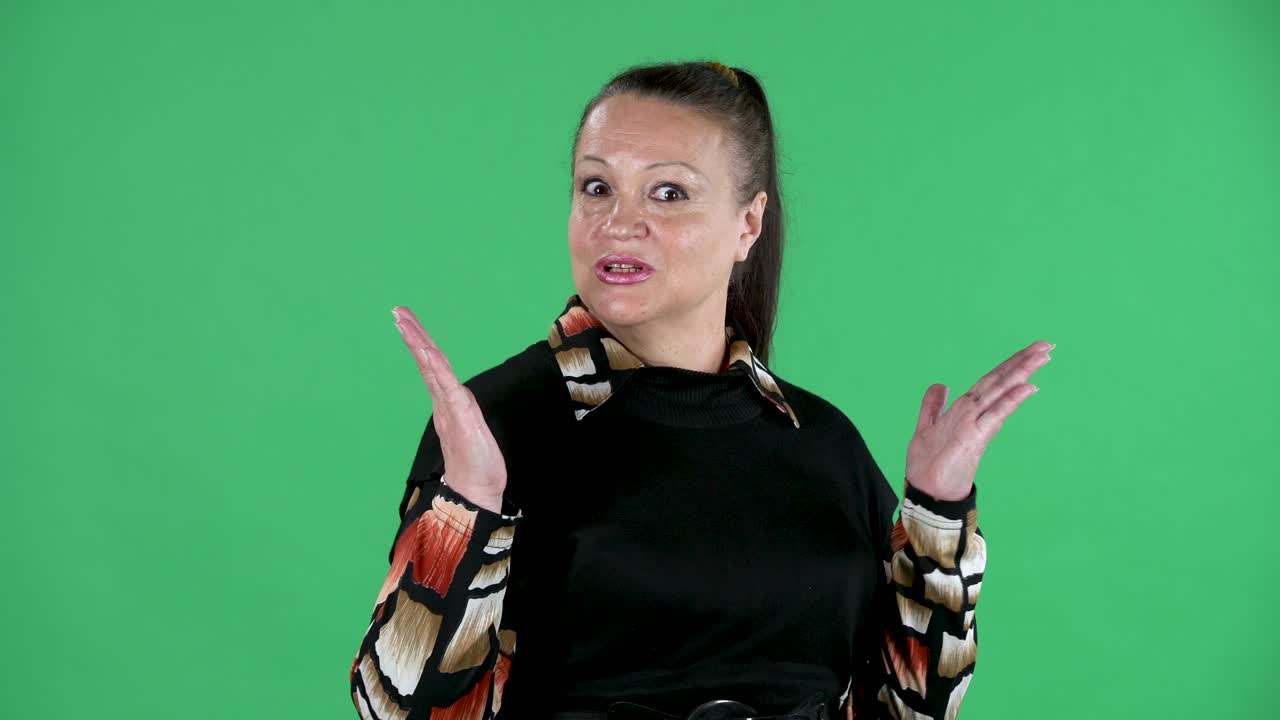 retrato mujer mayor mirando a la cámara instructivamente dice algo y hace un gesto con su dedo índice. abuela morena en vestido negro en pantalla verde en el estudio. cerca
