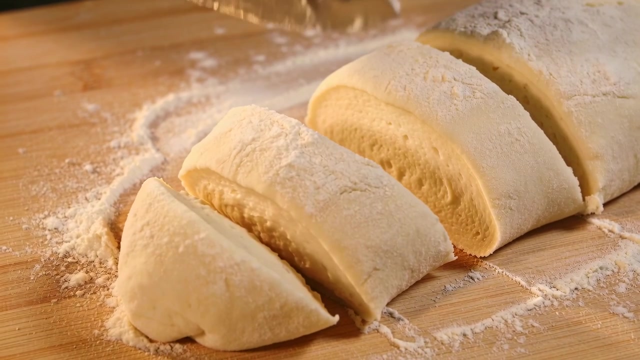Iniziando il primo taglio, mano nuda che guida il coltello attraverso l'impasto steso su un tagliere infarinato, preparando i dischi